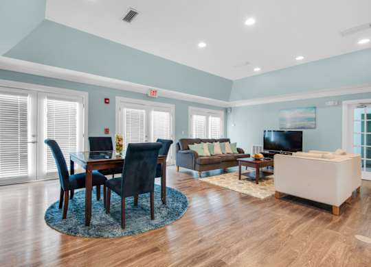 A modern clubhouse with tables and a lounge area with a TV at Crystal Lake in Pensacola, Florida.