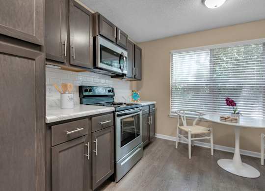A kitchen with brown cabinets, stainless-steel appliances, granite countertops, and a white tile backsplash at Crystal Lake in Pensacola, Florida.
