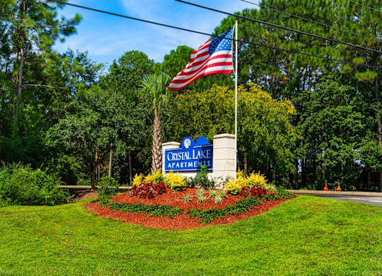 A sign for Crystal Lake Apartments is in front of  beautiful landscape in Pensacola, Florida.