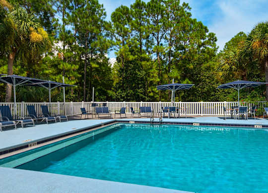 An outdoor swimming pool surrounded by lounge chairs and umbrellas at Crystal Lake in Pensacola, Florida.