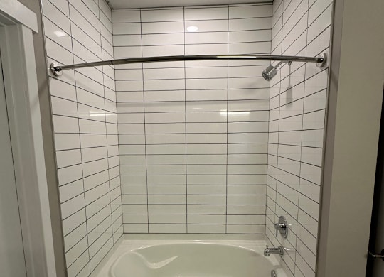 A white tiled shower with a white tub  at The Fitzroy Apartments in Birmingham, AL