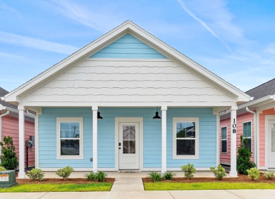 a blue house with a white roof and pink and blue houses at The Cottages at Foley Farms apartments in Foley, AL