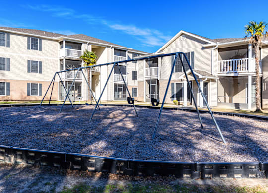 A playground with a swing set in front of apartment buildings  at Grande View Apartments in Biloxi, MS
