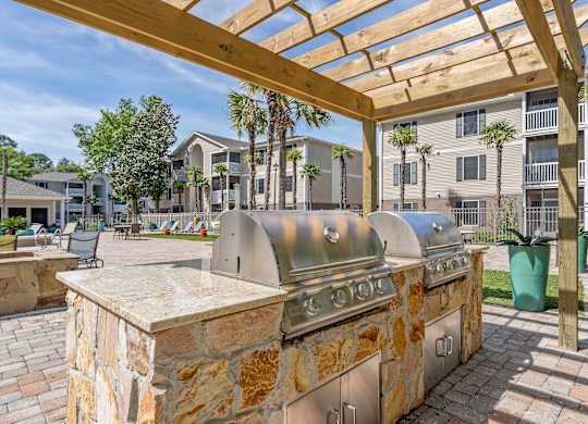 A stone BBQ grill is in the middle of a patio.