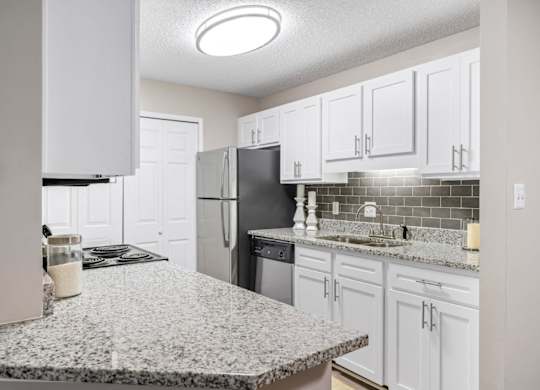 A kitchen with granite countertops, white cabinets, and a laundry closet at Summerchase at Riverchase in Hoover, Alabama.