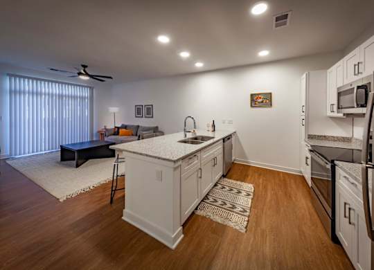 A kitchen with white cabinets, stainless steel appliances, wood-look flooring which opens into living room at Wesley Place Apartments in Indianapolis, IN
