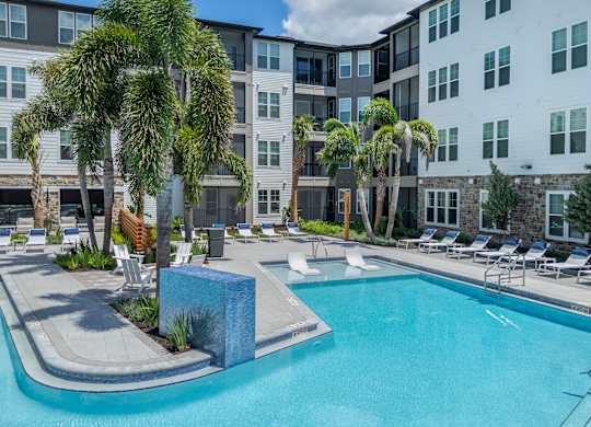 A swimming pool surrounded by palm trees and lounge chairs.