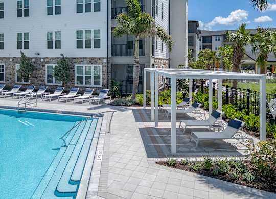 A pool with lounge chairs and a white pergola.