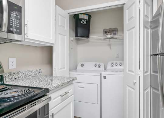 A kitchen with granite countertops, white cabinets, and a washer and dryer unit at Summerchase at Riverchase in Hoover, Alabama.