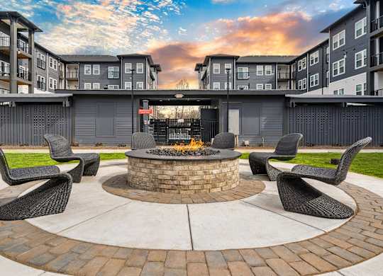 A fire pit sits in the middle of a brick patio surrounded by four chairs.