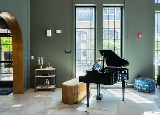 A grand piano sits in a room with a green wall and a large arched doorway.
