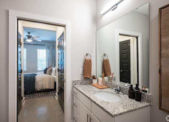 A bathroom with a large mirror and a bedroom visible through the door.
