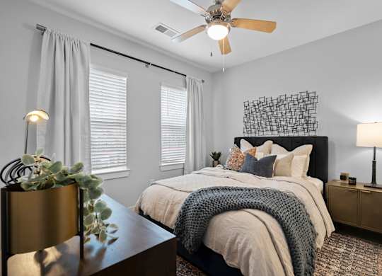 A bedroom with a bed, a ceiling fan, and a plant on a table.