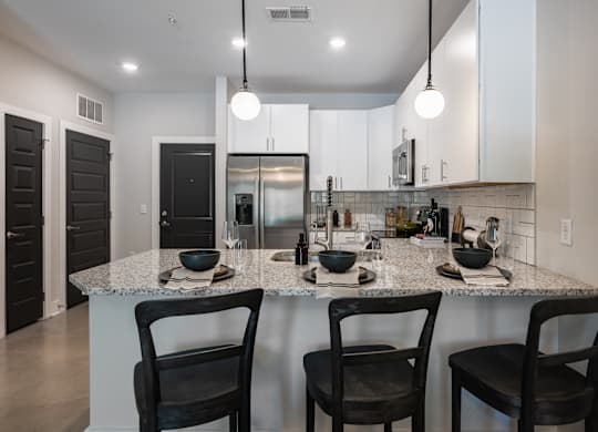 A kitchen with a granite countertop and black chairs.