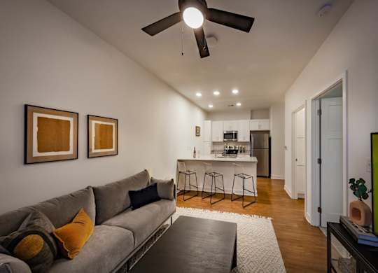 A living room with a ceiling fan and wood-look flooring that opens to the kitchen at Wesley Place Apartments in Indianapolis, IN.