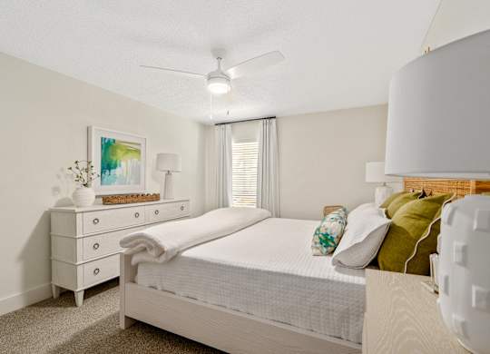 A white bedroom with a bed, nightstand, and a ceiling fan.