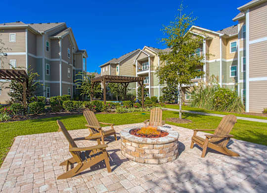 A fire pit sits in the middle of a brick patio surrounded by four chairs.