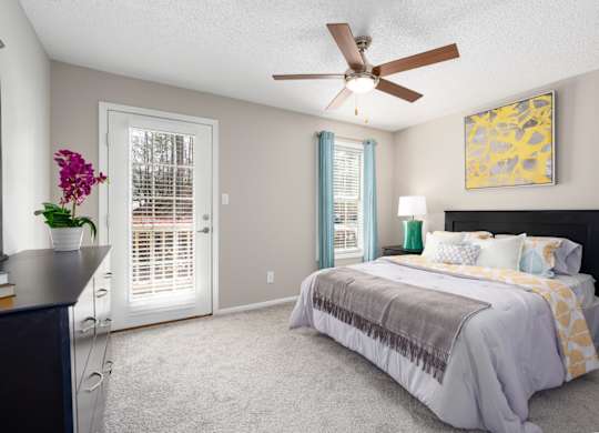A bedroom with patio access, carpet flooring, ceiling fan, and a window at Summerchase at Riverchase in Hoover, Alabama.