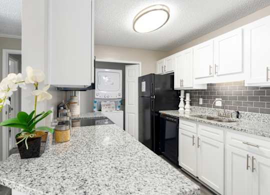 A kitchen with granite countertops, white cabinets, and a stackable washer and dryer at Summerchase at Riverchase in Hoover, Alabama.