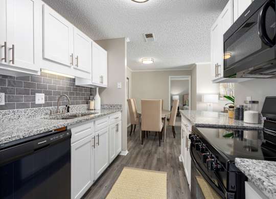 A kitchen with black appliances, granite countertops, white cabinets, and tile backsplash at Summerchase at Riverchase in Hoover, Alabama.