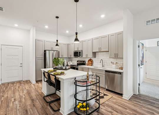 Island kitchen with custom cabinets, stainless steel appliances, and pendant lighting at Tapestry University Park Apartments in Sarasota, FL