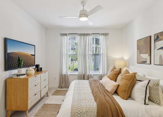 A bedroom with a large bed, a dresser, a ceiling fan, and a painting on the wall.