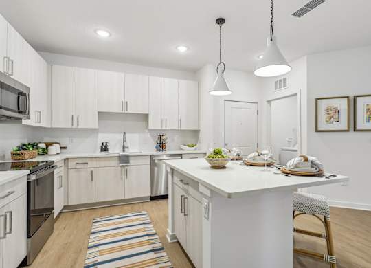 A kitchen with white cabinets and a white island with a bowl of fruit on it.