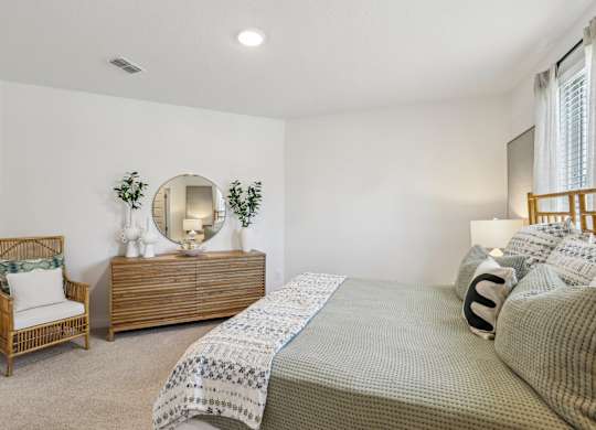 A bedroom with a bed, chair, and mirror.