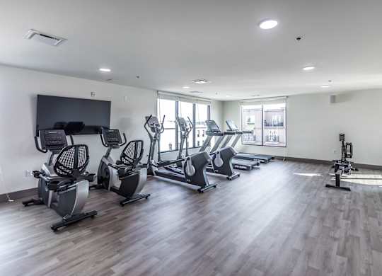 a gym with cardio equipment on a wooden floor and windows