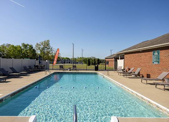 A large outdoor swimming pool surrounded by lounge chairs and a fence.