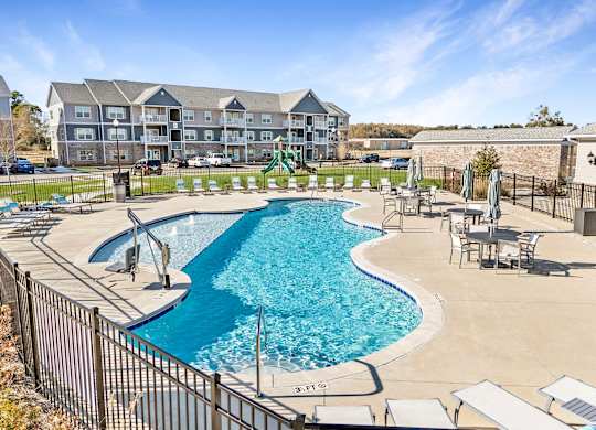 A large swimming pool surrounded by a fence and chairs.