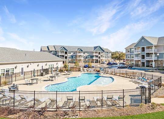 A large swimming pool surrounded by a black fence and lounge chairs.