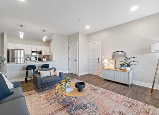 A modern living room with a grey sofa, a round table with a plant on it, and a white cabinet with a lamp on top.