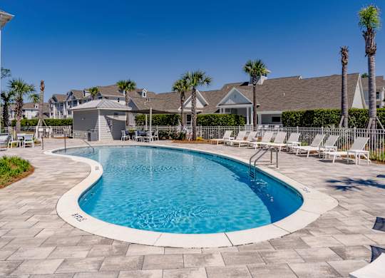 A swimming pool surrounded by a stone patio and lounge chairs.