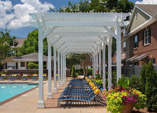 A white pergola is over a pool with blue chairs.