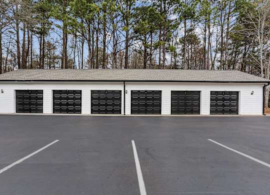 A large white building with black garage doors in the middle of a parking lot.
