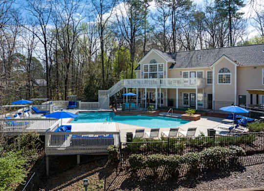 Large outdoor pool surrounded by trees, lounge chairs and umbrellas with staircase access to the clubhouse at Summerchase at Riverchase in Hoover, Alabama.