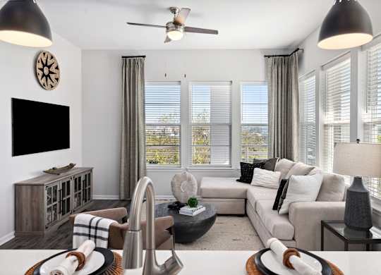 A living room with a large couch, a television, and a ceiling fan.