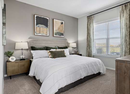 A bedroom with a large bed, two lamps, and two pictures on the wall.