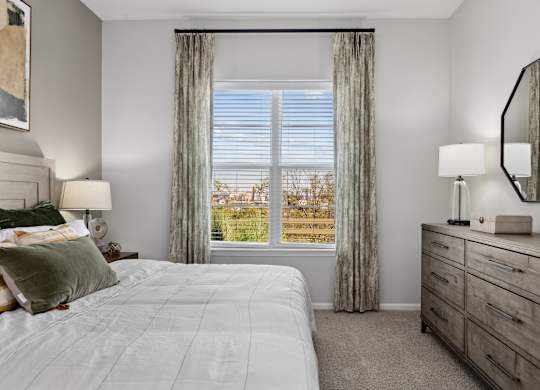 A well-lit bedroom with a large bed and a dresser with a mirror.