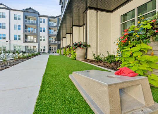a sidewalk in front of an apartment building with grass and flowers
