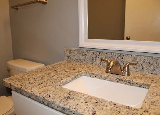 A bathroom with a granite countertop and framed mirror at The Avery at Auburn Apartments in Auburn, AL