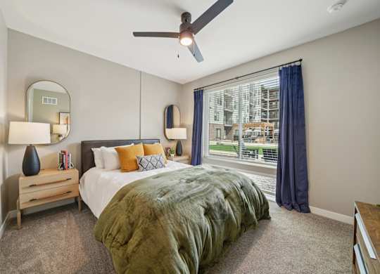 A bedroom with a bed, a ceiling fan, and a window with a view of a building outside.