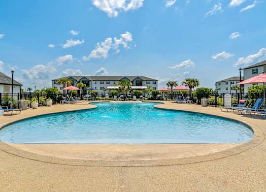 a resort style pool with lounge chairs and umbrellas at the whispering winds apartments in pear
