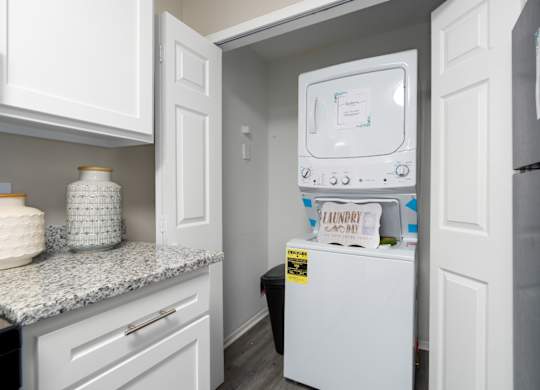 A kitchen with granite countertops, white cabinets, and a washer and dryer unit at Summerchase at Riverchase in Hoover, Alabama.