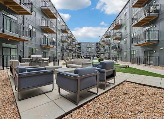 A patio with couches and chairs is surrounded by apartment buildings.