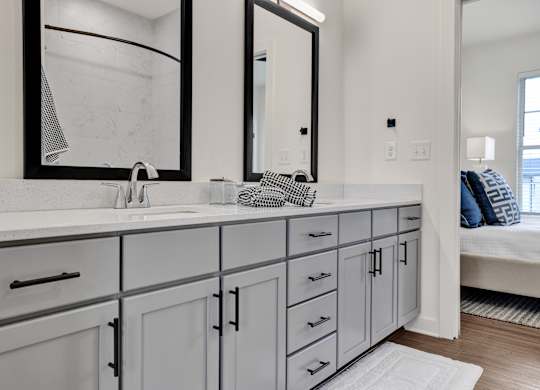 Modern bathroom with double vanity, gray cabinets, quartz countertops, and designer plank flooring at West Row Lofts and Townhomes in Birmingham, AL.