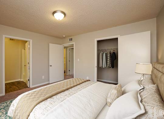 A bedroom with a large bed and a closet with clothes hanging.
