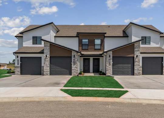 A large, modern house with a front yard and two garages.