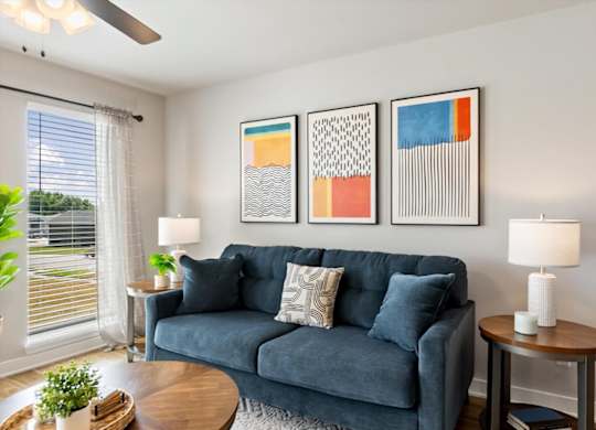 A living room with a blue couch and three framed artworks on the wall.